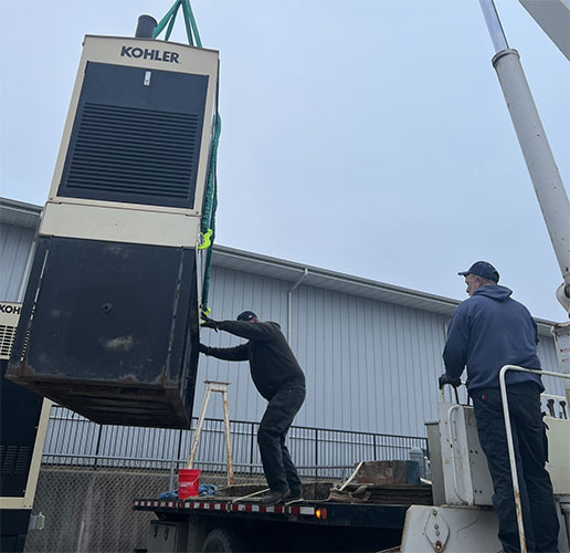 Workers lift a Kohler generator unit using a crane